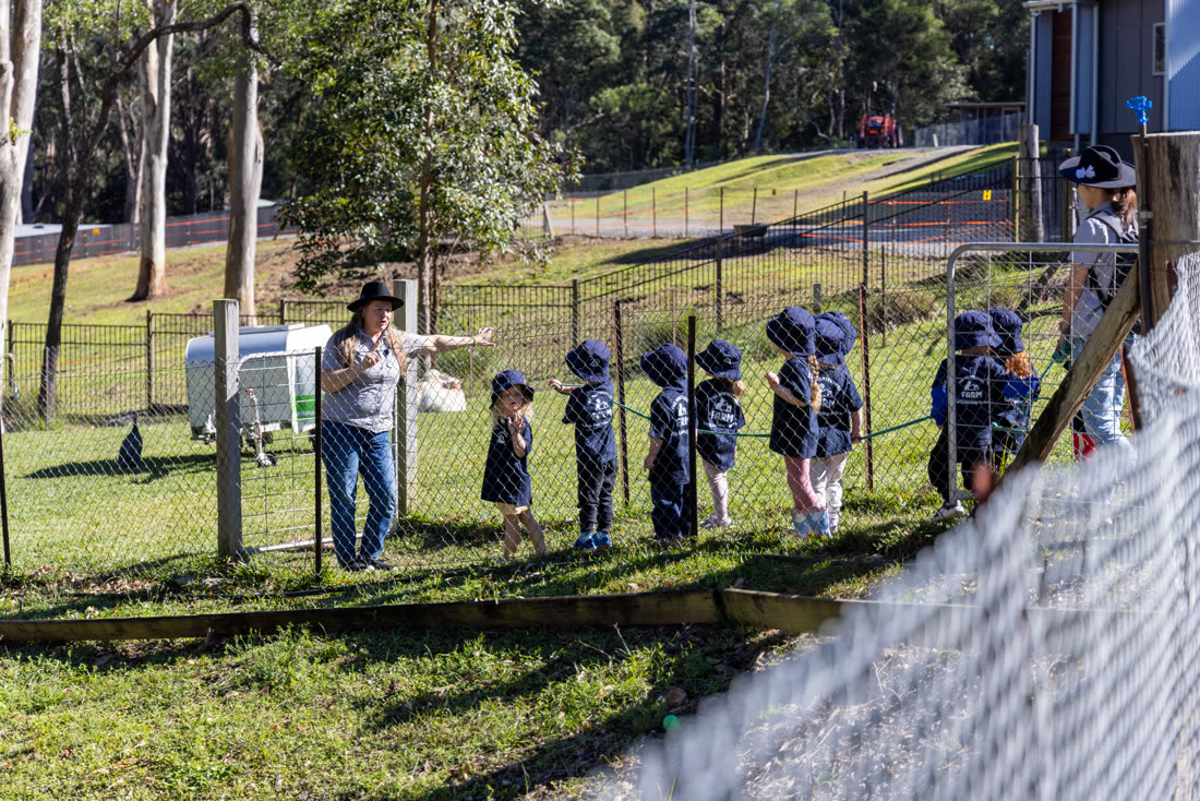 Children lined up along the paddock fence with an educator